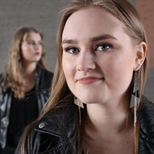 Lähikuvassa nainen, jolla päällä hopeat isot Kiila-korvakorut. Taustalla toinen nainen joka katsoo toisaalle.